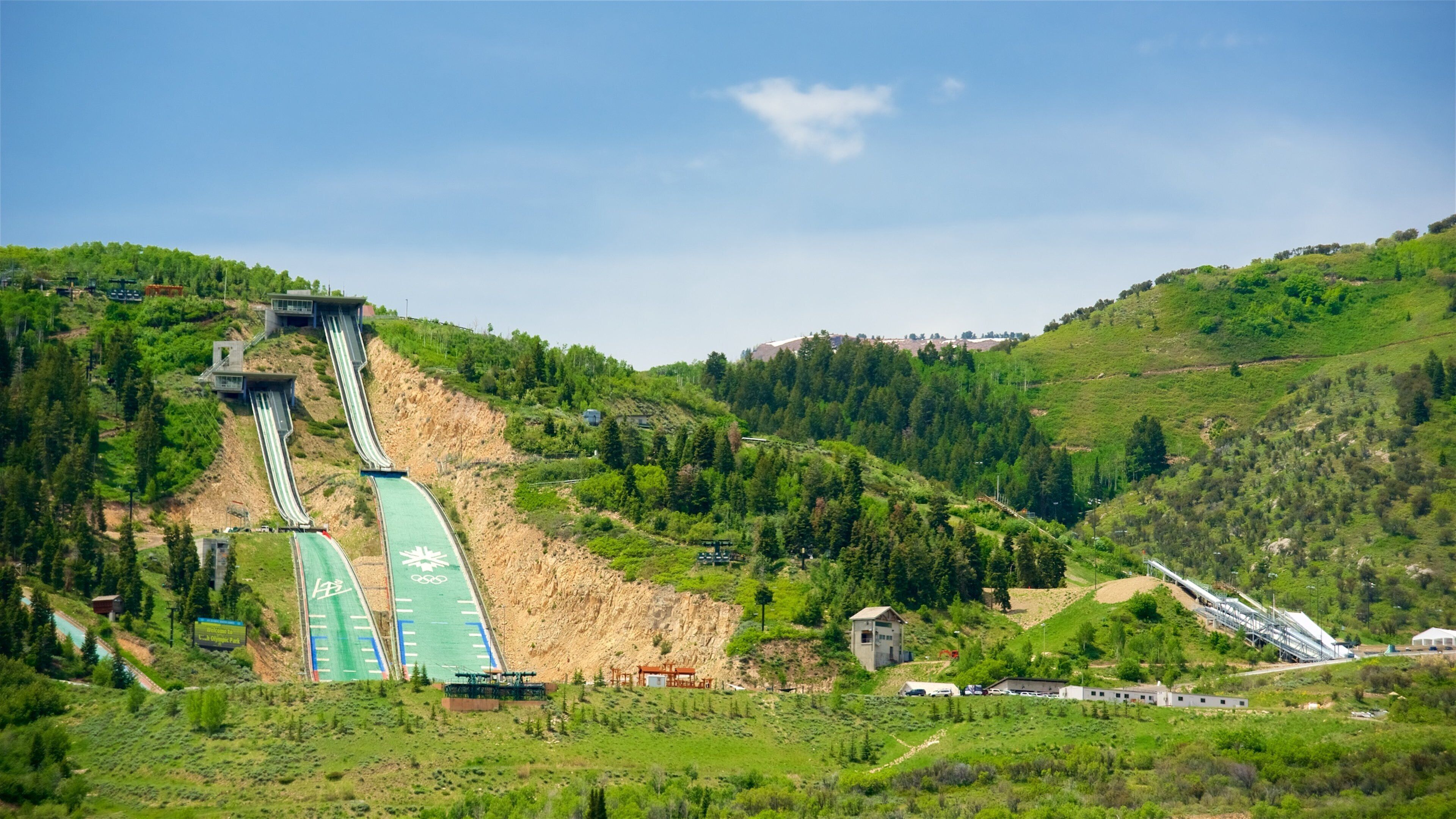 A hydroelectric dam with two large water channels, surrounded by lush green hills and a clear blue sky.