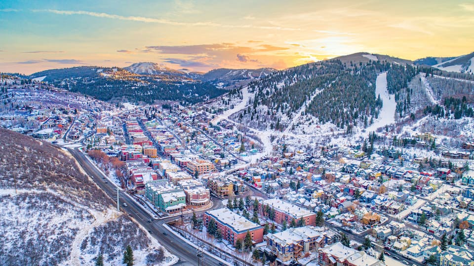 A snow-covered town with colorful buildings, surrounded by mountains and a ski slope.