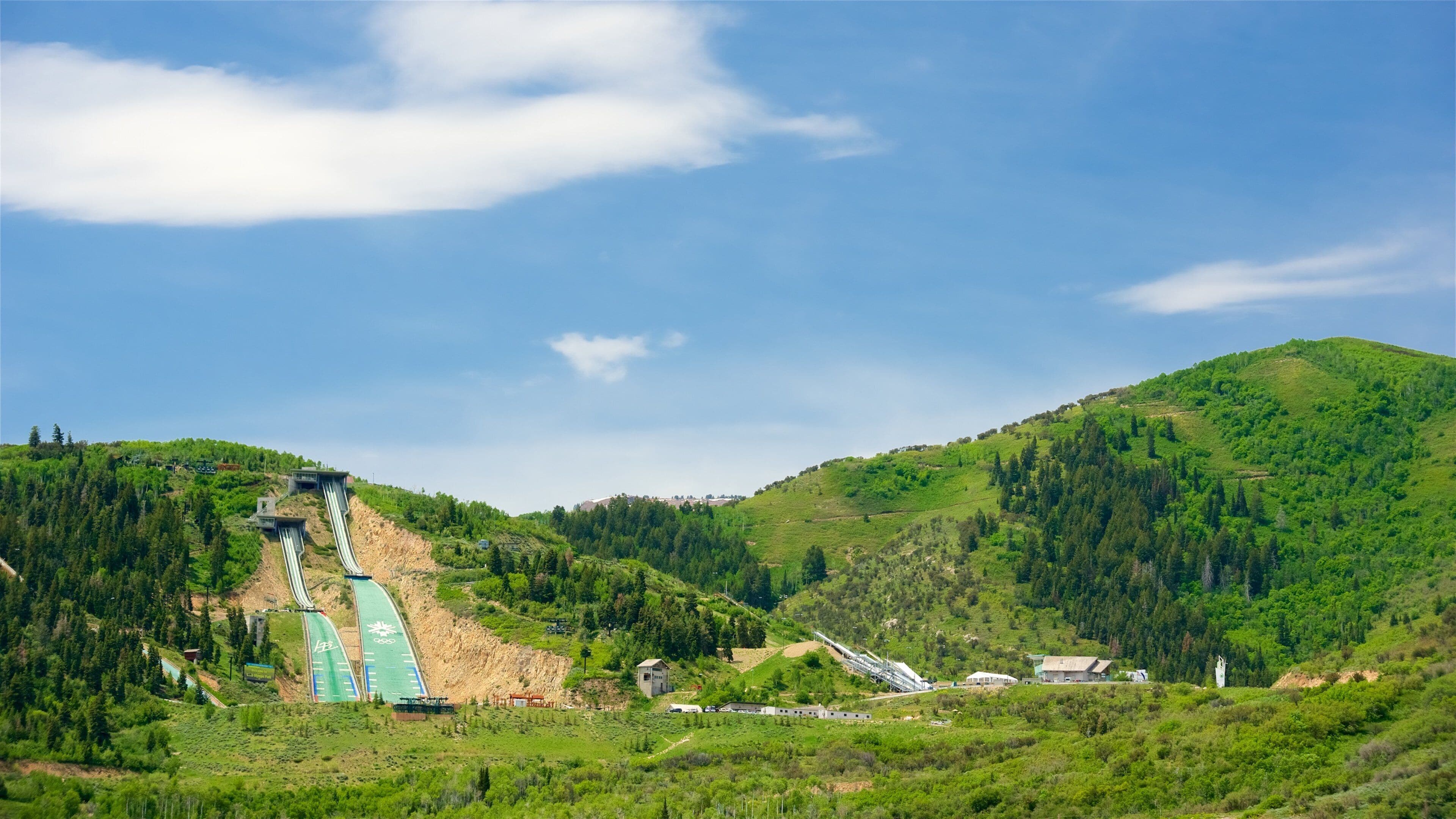 A hydroelectric dam with a water channel, surrounded by lush green hills and a clear blue sky.