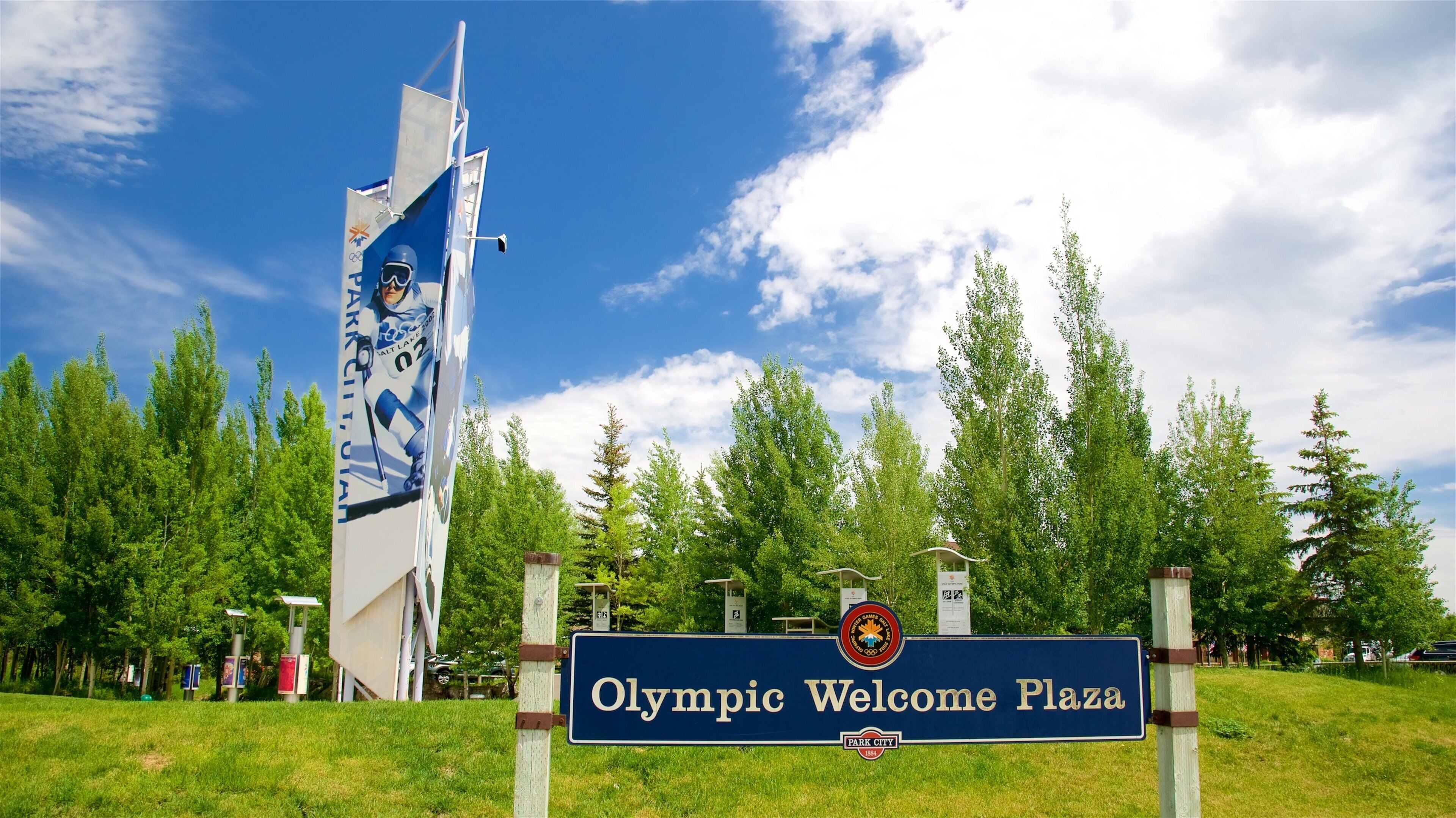 An Olympic Welcome Plaza sign with a large sculpture in the background.
