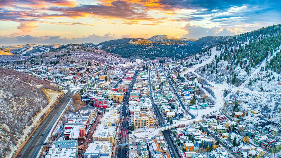 Eine verschneite Stadt mit Bergen im Hintergrund und einem Sonnenuntergangshimmel.