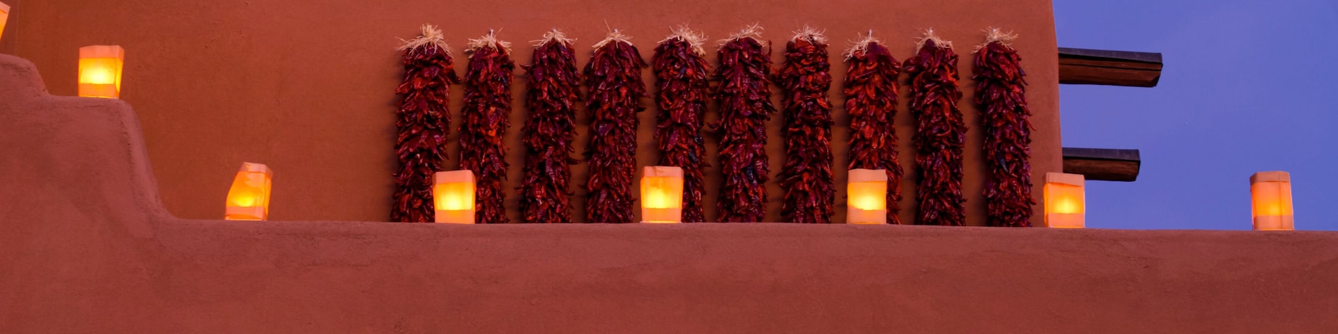 A building with a row of lit lanterns and decorative garlands against a twilight sky.