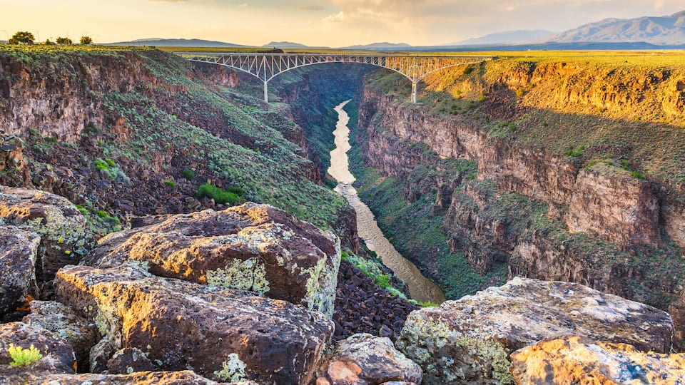 A bridge over a deep canyon with rocky terrain and a river.