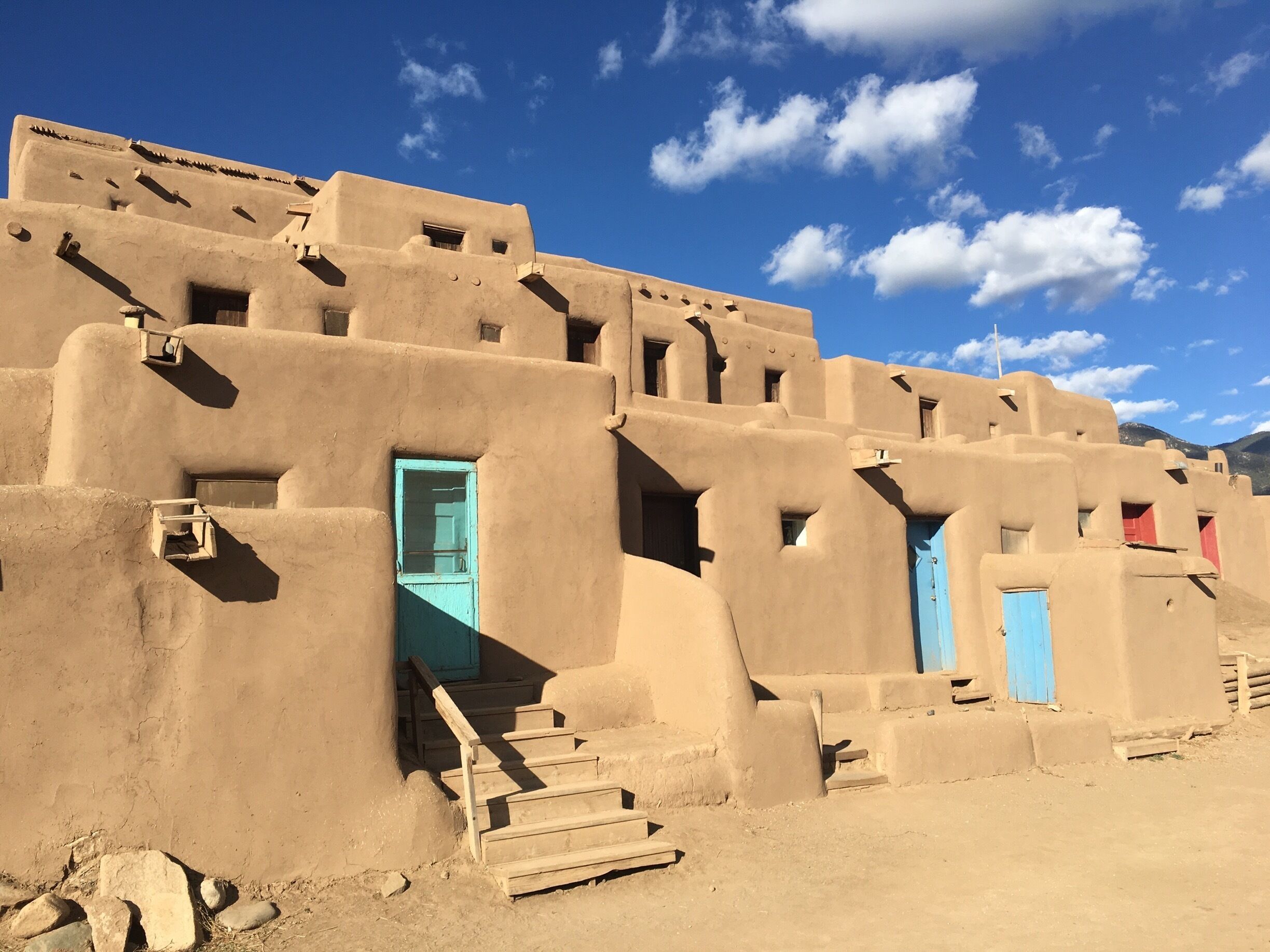 A traditional adobe building with blue doors and a wooden staircase.