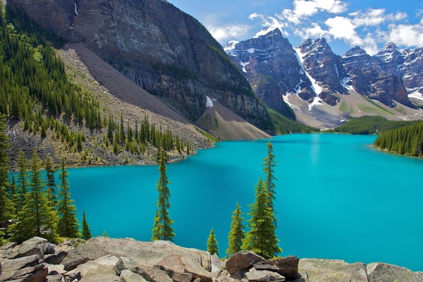 Ein türkisblauer See, umgeben von Bergen und dichten Wäldern.