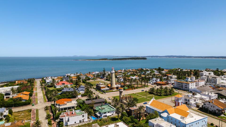 A coastal town with a lighthouse, houses, and palm trees.