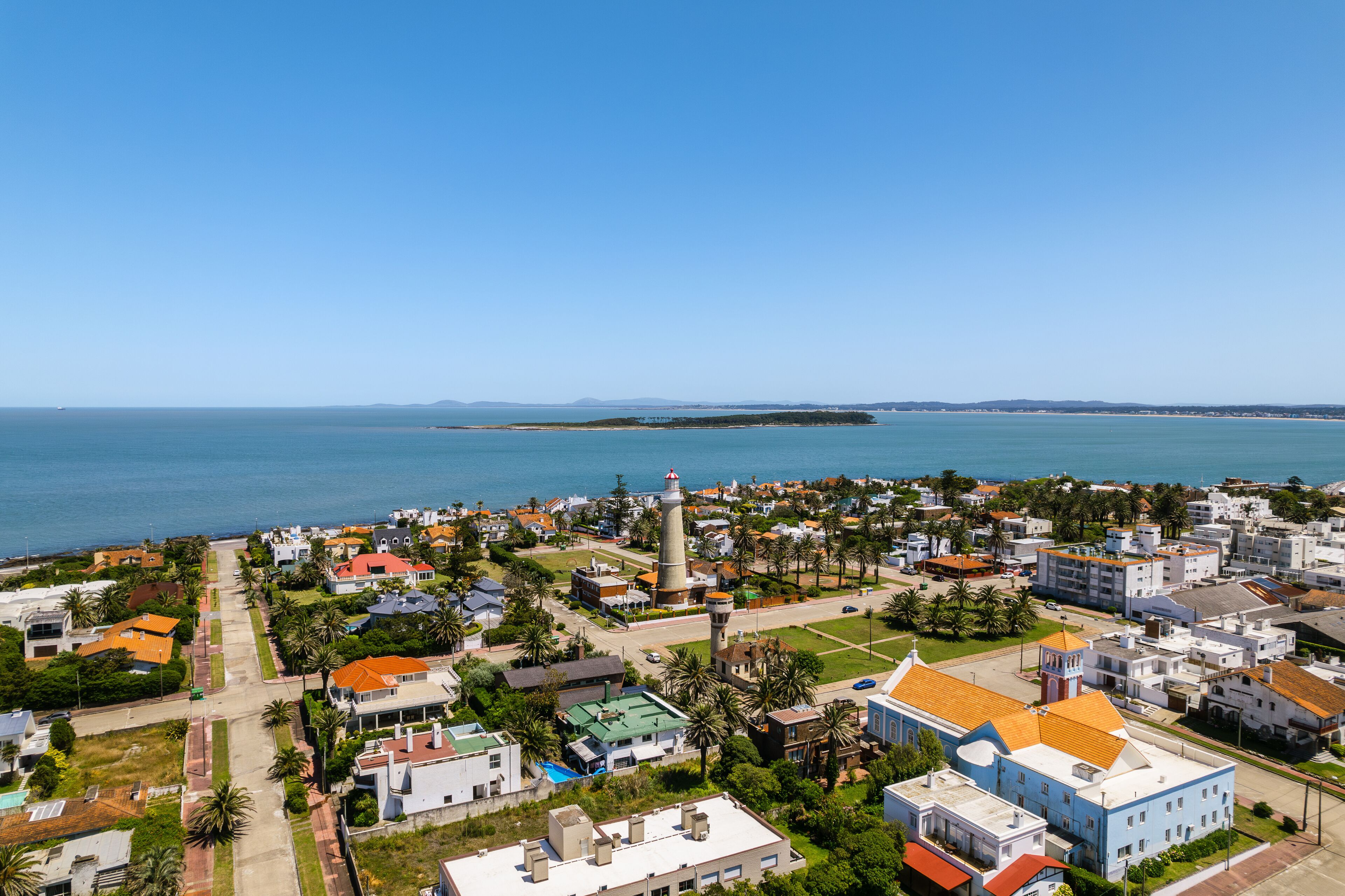 A coastal town with a lighthouse, houses, and palm trees.
