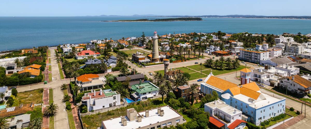 A coastal town with a lighthouse, houses, and palm trees.
