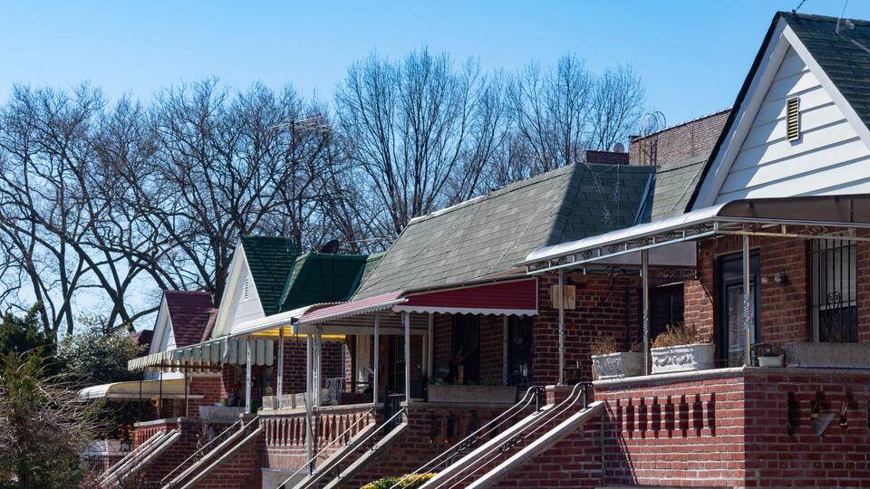 A row of brick houses with a covered porch and a staircase leading to the entrance.