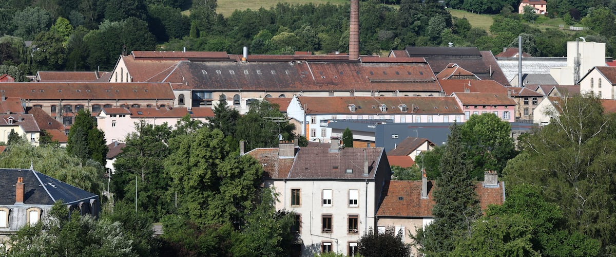 A town with historic buildings, a prominent church steeple, and a hill with a house in the background.