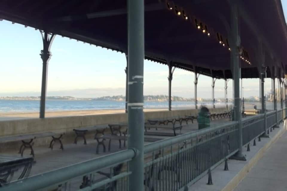 A covered walkway with benches overlooking a beach.