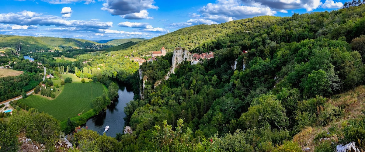 A river winding through a lush valley with a castle on a cliff, surrounded by dense forests and rolling hills.