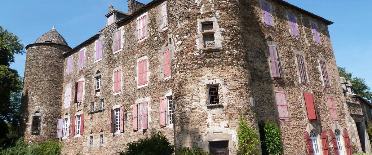A historic stone building with red shutters and a round tower.