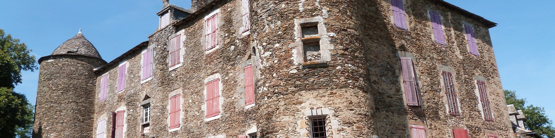 A historic stone building with red shutters and a round tower.