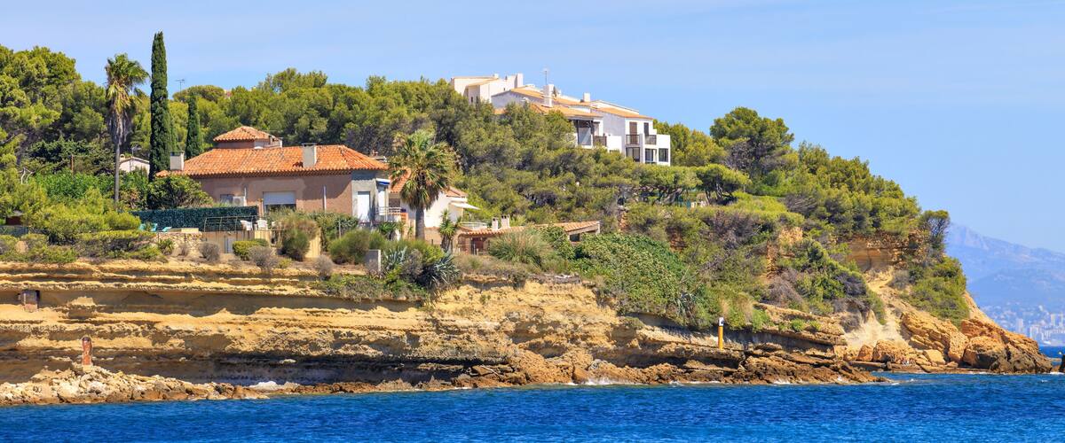 A coastal town with Mediterranean architecture, rocky cliffs, and a clear blue sea.