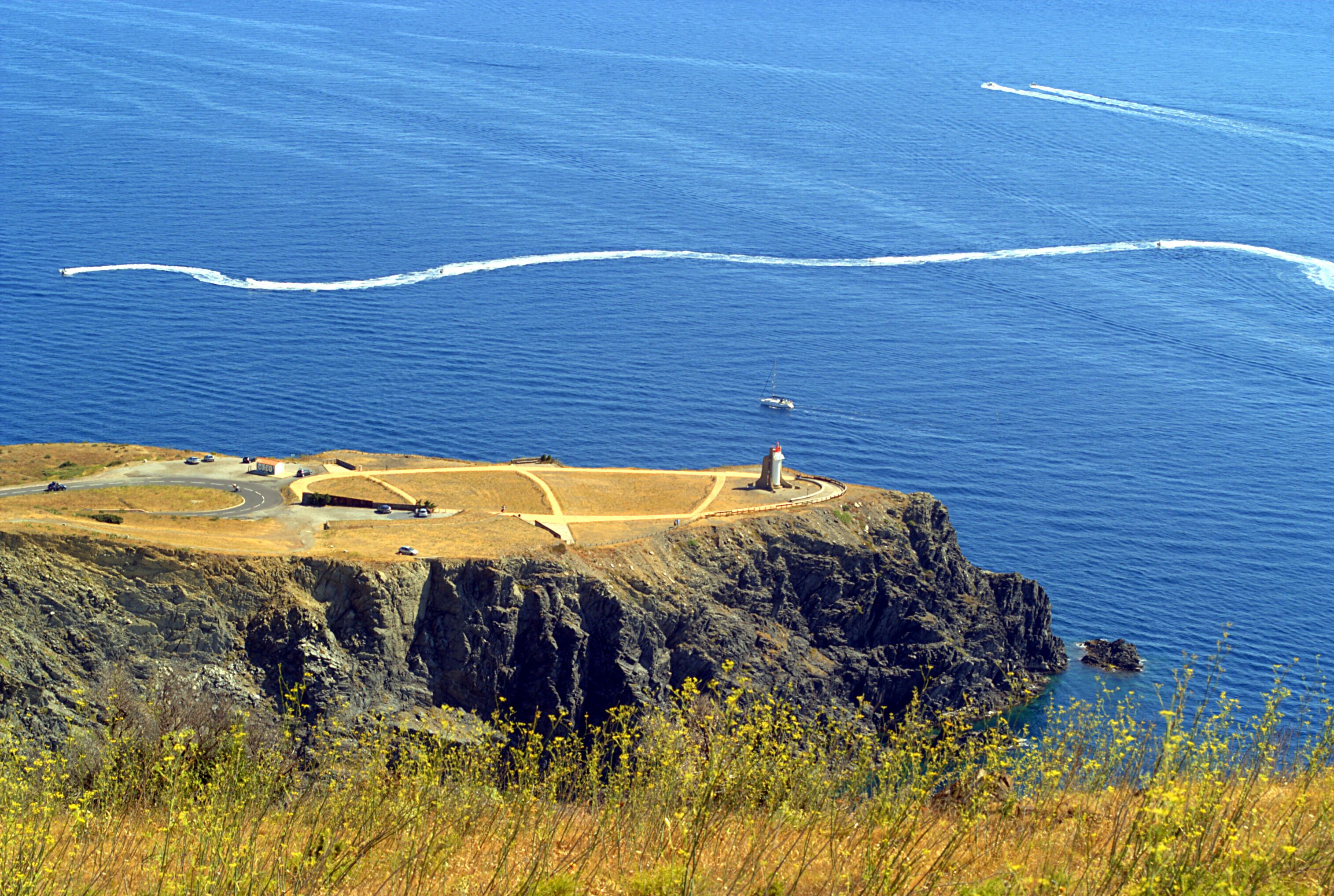 A coastal landscape with a lighthouse, winding roads, and a sailboat on the water.