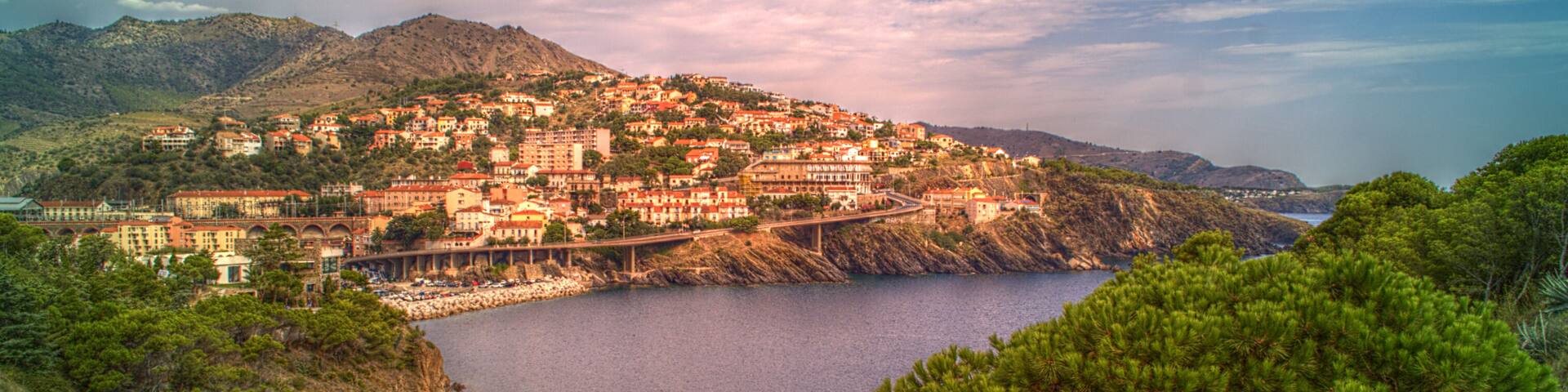 A coastal town with buildings on a hillside, a bridge, and a body of water.