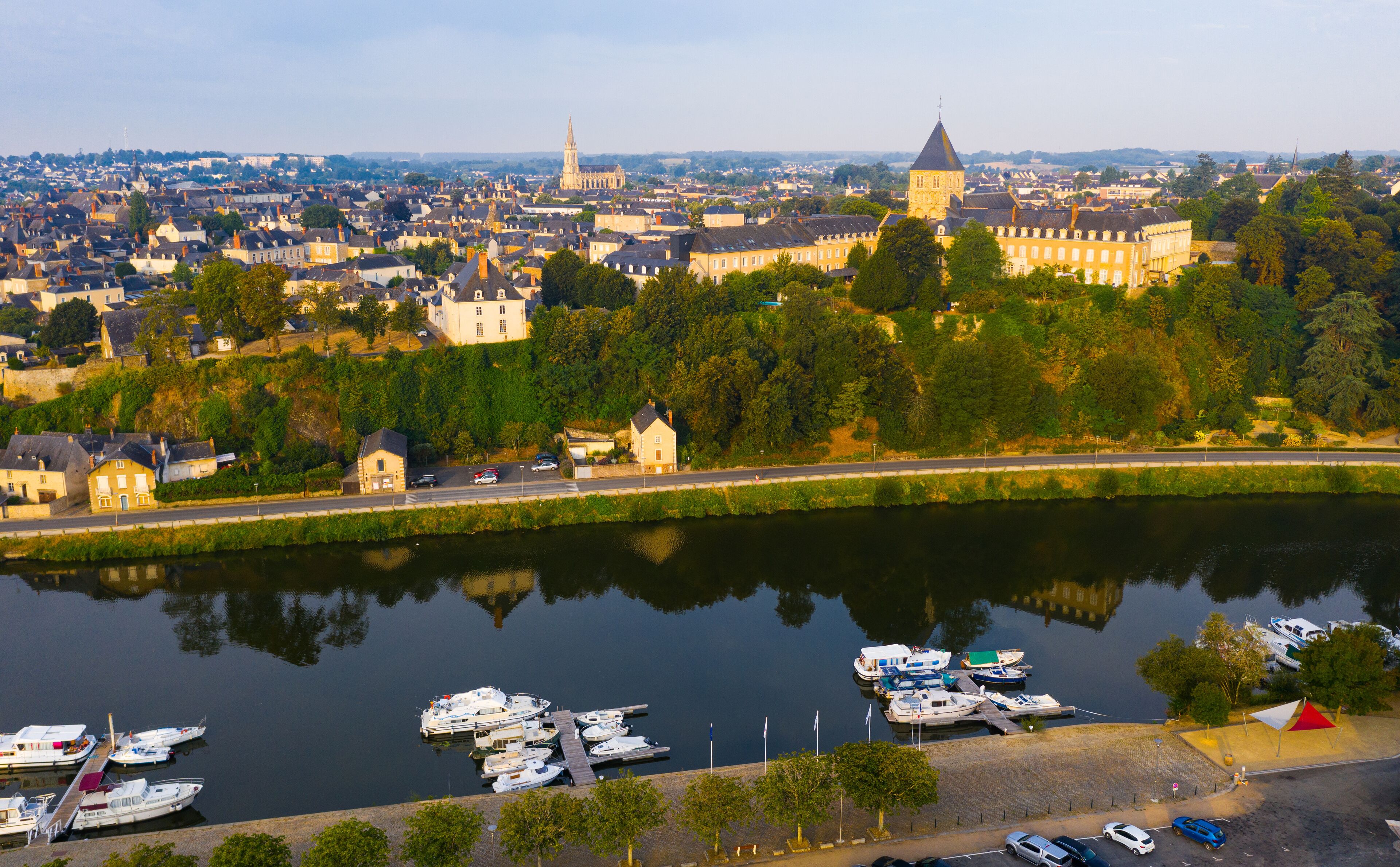 A river with boats docked on the right, a bridge in the middle, and a cityscape with historic buildings and a church in the background.