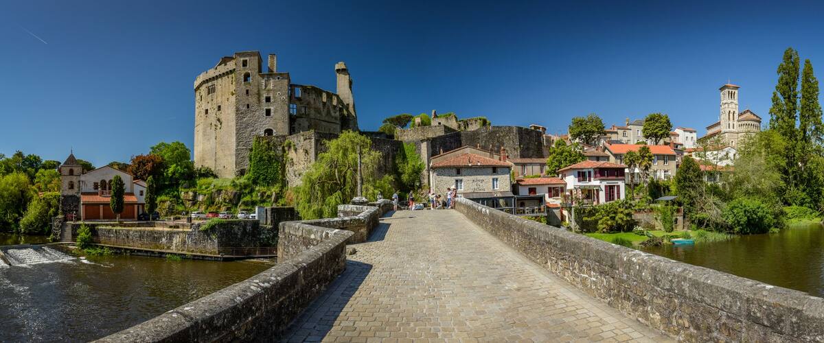 A historic stone bridge over a river, leading to a castle and a church.