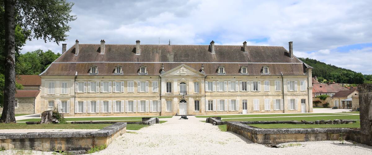 A large, historic building with a symmetrical facade, a central entrance, and a gravel courtyard.