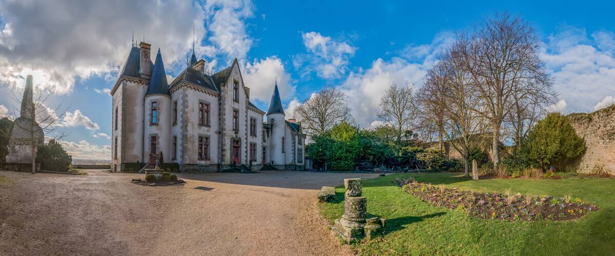 A historic castle with multiple towers, a gravel courtyard, and a well-maintained garden with flowering plants.