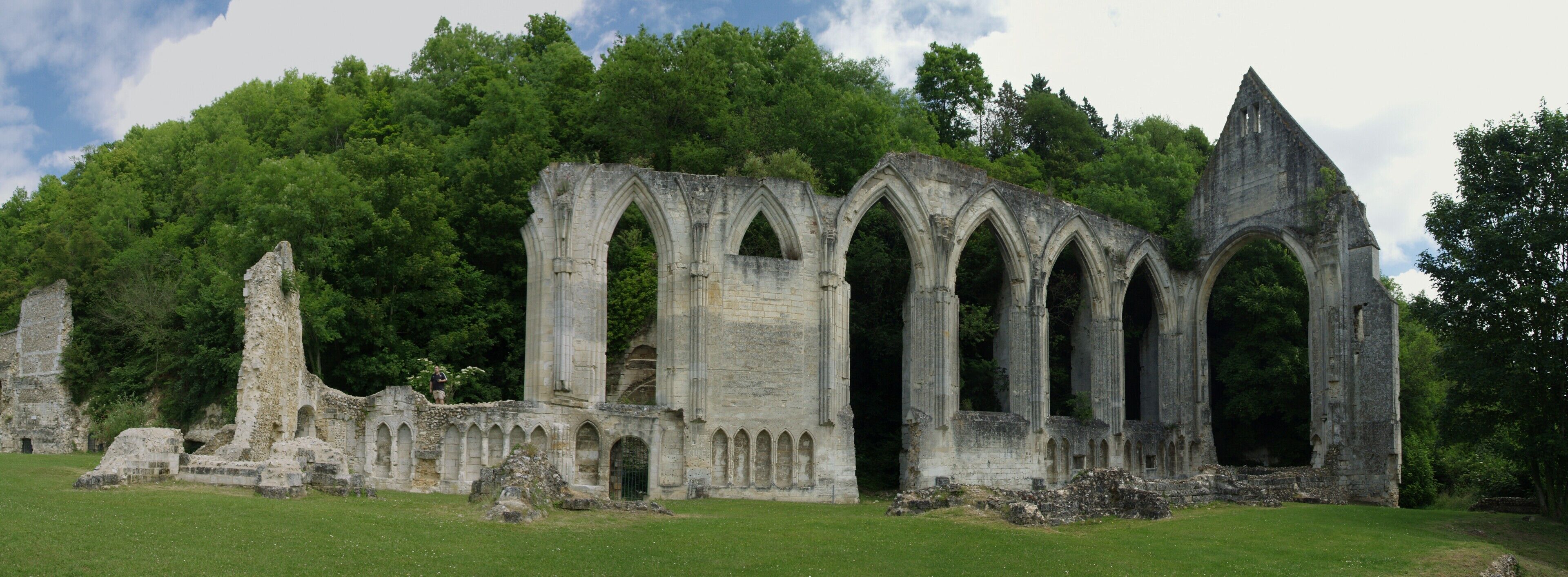 A historic stone structure with arches and ruins, surrounded by lush green trees.