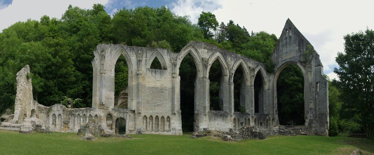 A historic stone structure with arches and ruins, surrounded by lush green trees.