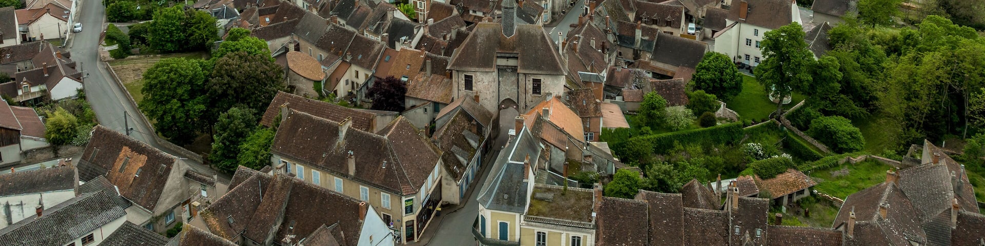 Aerial view of Ainay le Chateau from the east, small medieval town in Allier department in France with ramparts and city gate clock tower cloudy sky