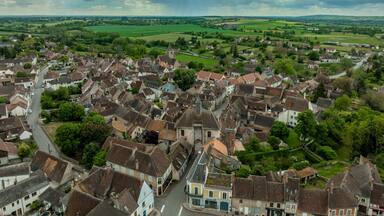 Aerial view of Ainay le Chateau from the east, small medieval town in Allier department in France with ramparts and city gate clock tower cloudy sky