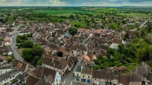 Aerial view of Ainay le Chateau from the east, small medieval town in Allier department in France with ramparts and city gate clock tower cloudy sky