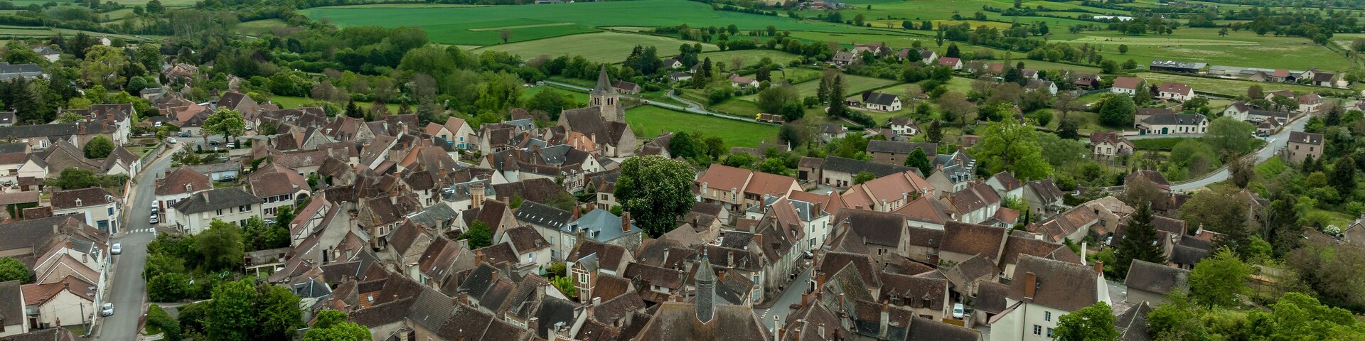 Aerial view of Ainay le Chateau from the east, small medieval town in Allier department in France with ramparts and city gate clock tower cloudy sky
