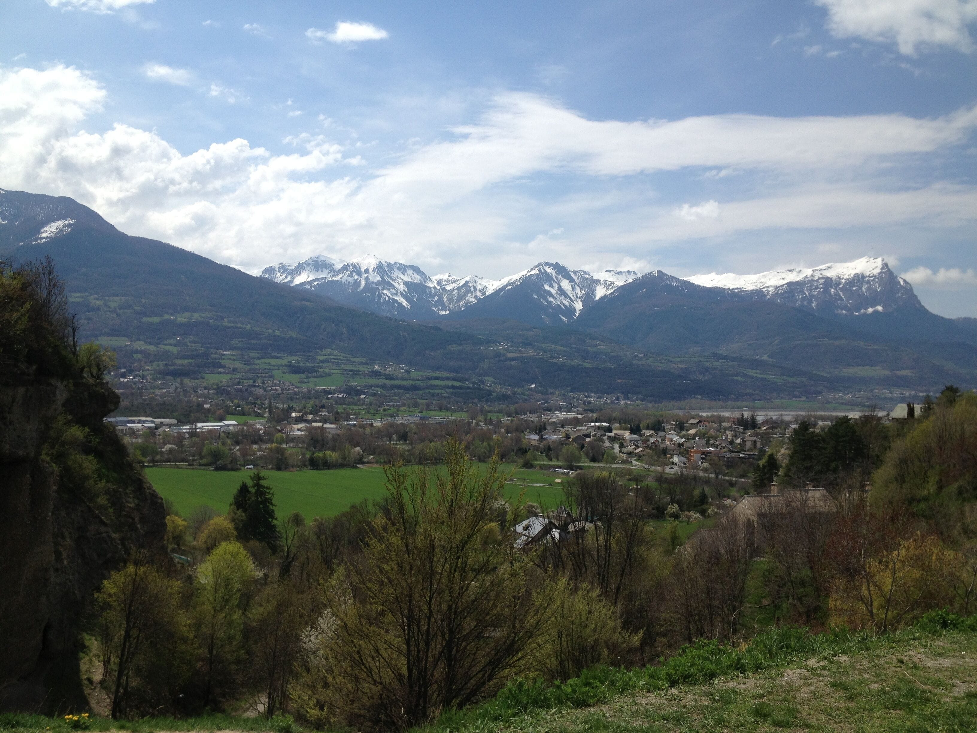 A valley with snow-capped mountains, a town, and green fields.