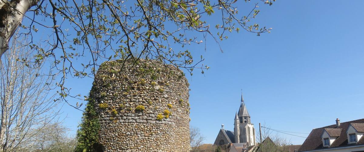 A stone tower with a church in the background.
