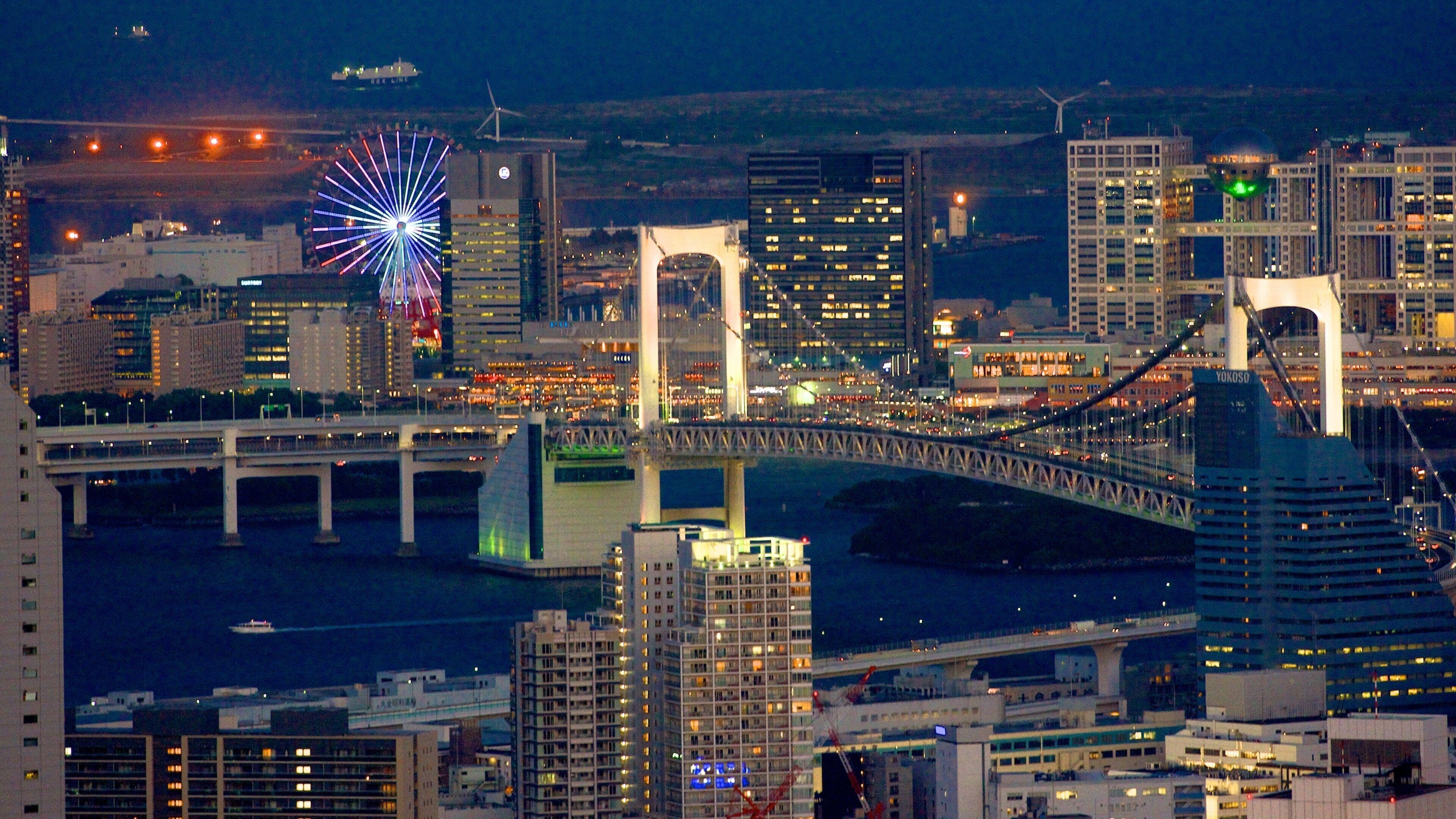 A cityscape at night with a prominent bridge, illuminated buildings, and a colorful Ferris wheel.