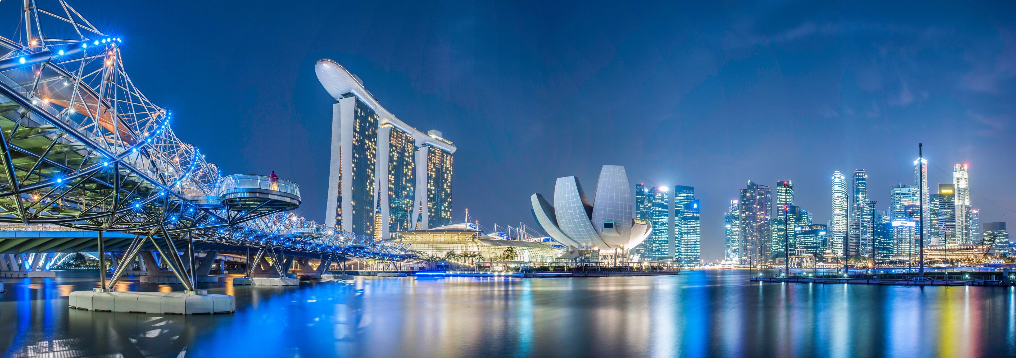 Uma paisagem urbana noturna com uma roda-gigante em destaque, um edifício moderno característico com telhado curvo e um conjunto de arranha-céus.