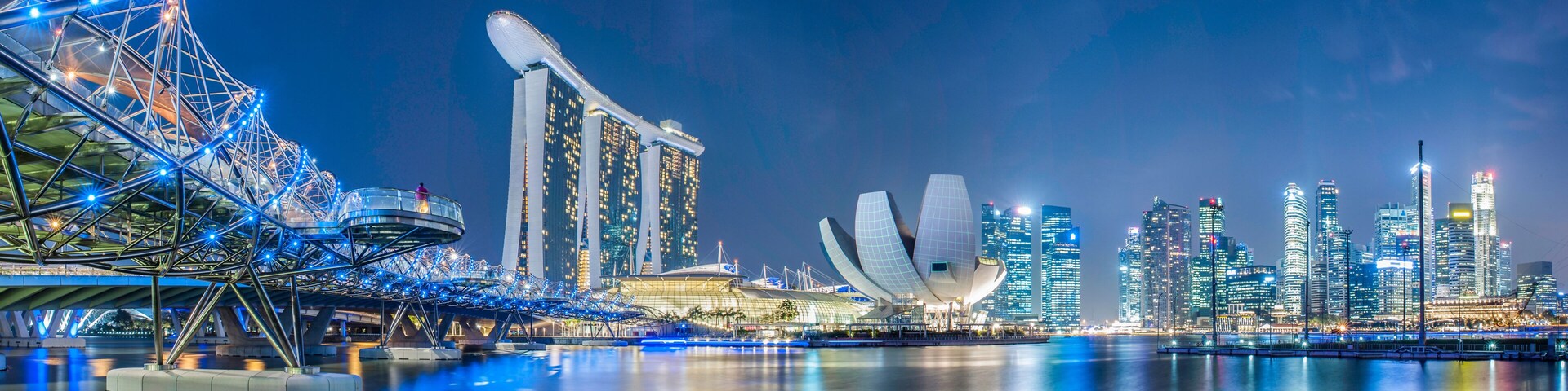 Uma paisagem urbana noturna com uma roda-gigante em destaque, um edifício moderno característico com telhado curvo e um conjunto de arranha-céus.