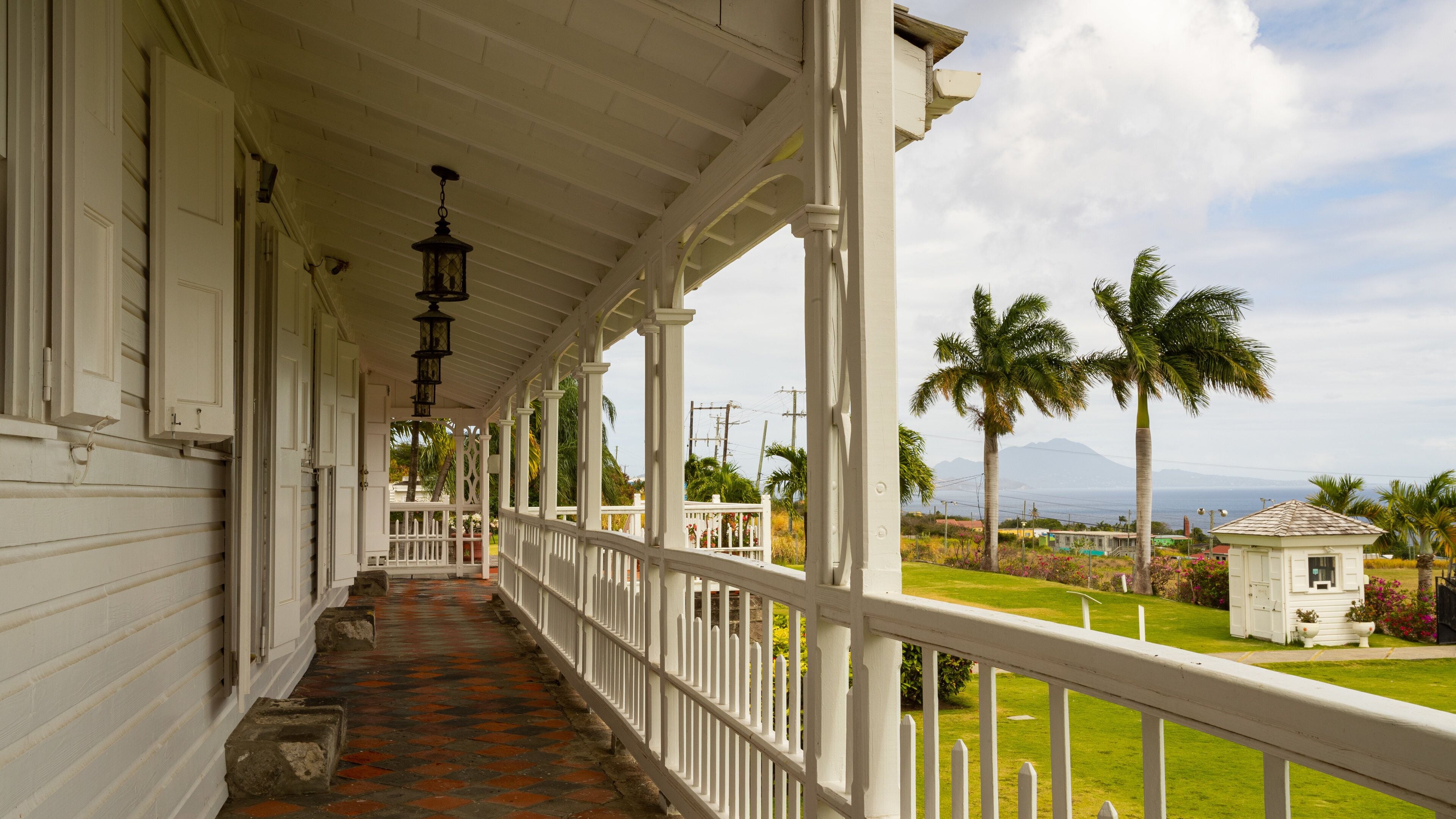 A covered porch with a tiled floor, white railings, and a view of palm trees and mountains in the distance.