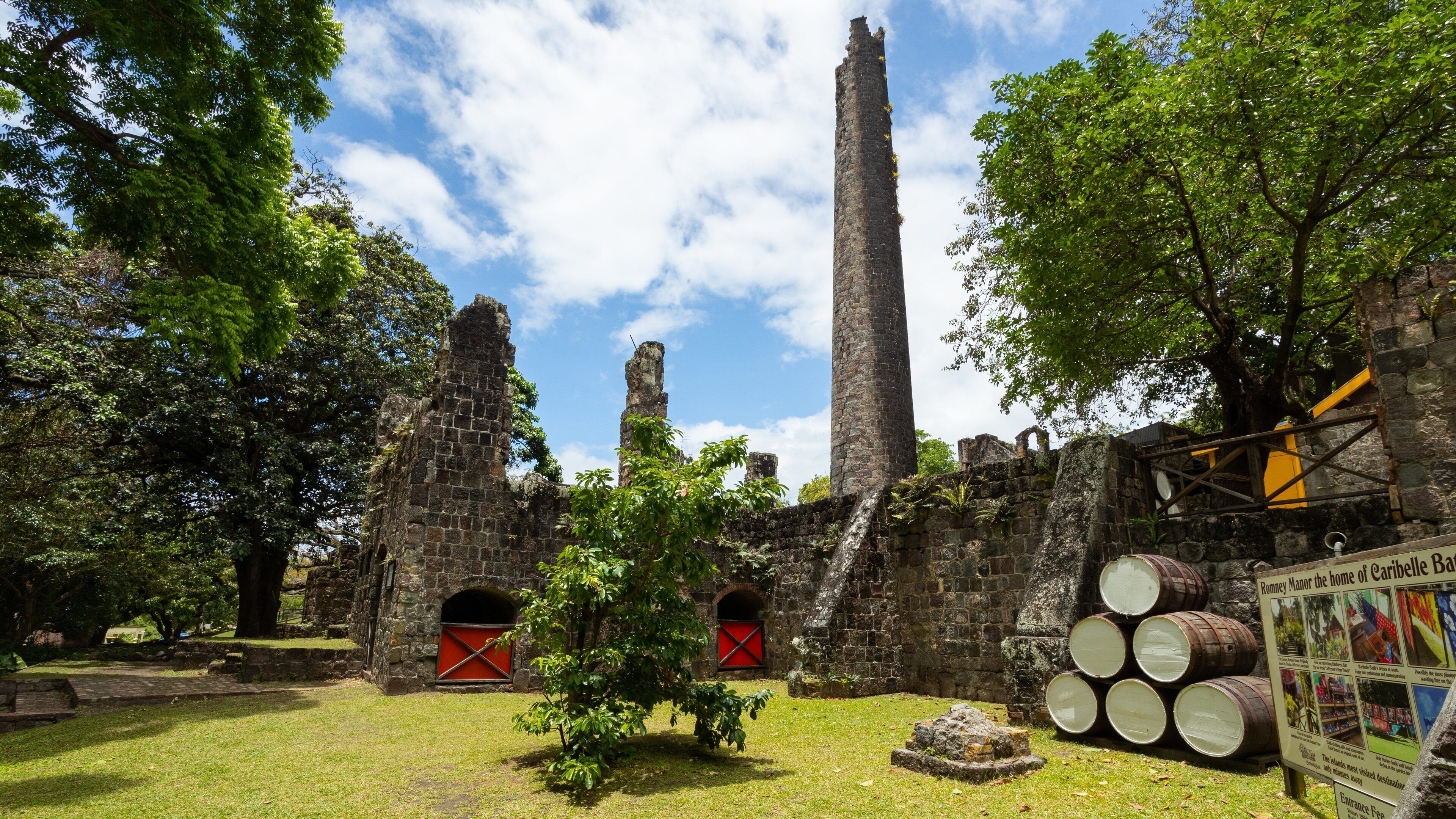 An ancient stone structure with ruins, including a tall tower and arched openings, surrounded by lush greenery.