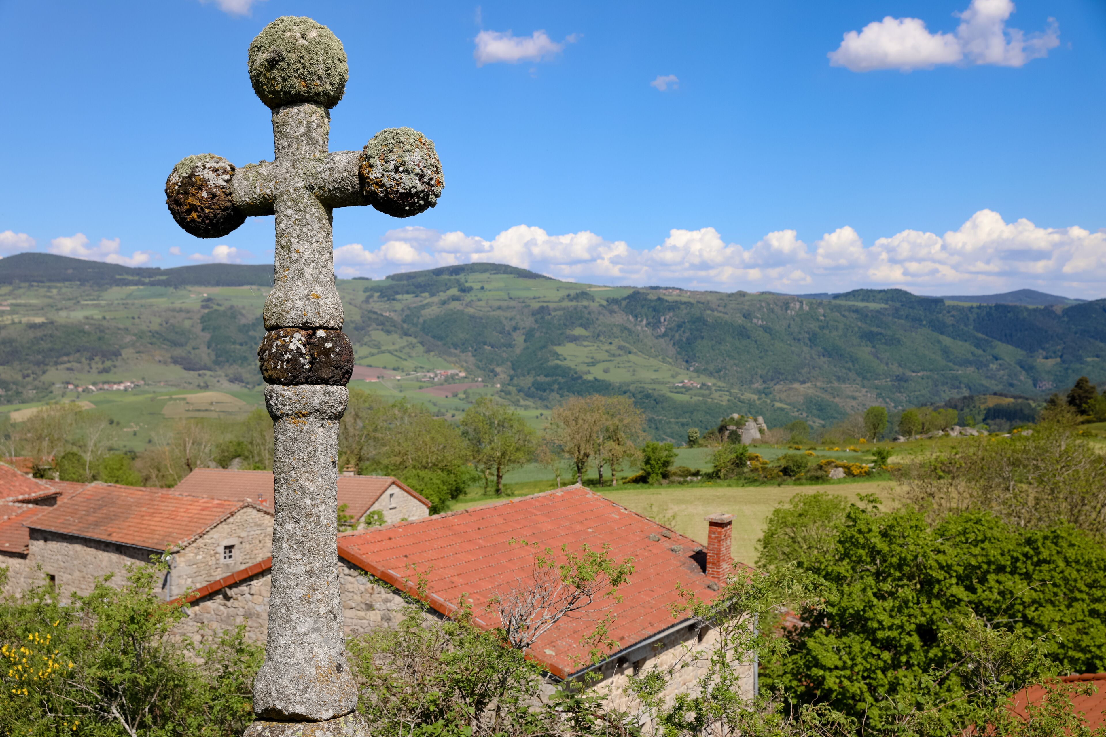 Croix de pierre au dessus d'un village. Paysage de campagne vallonnée l'été en Auvergne. Nature, collines, forêts, champs et prairies de Haute Loire en France.