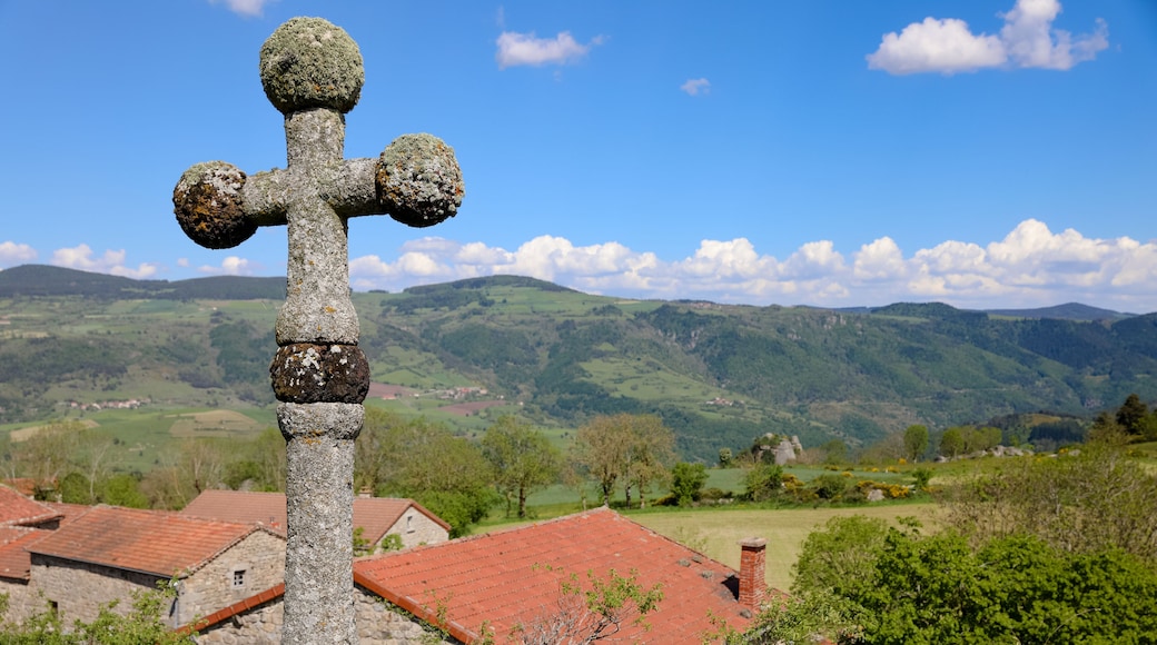 Croix de pierre au dessus d'un village. Paysage de campagne vallonnée l'été en Auvergne. Nature, collines, forêts, champs et prairies de Haute Loire en France.