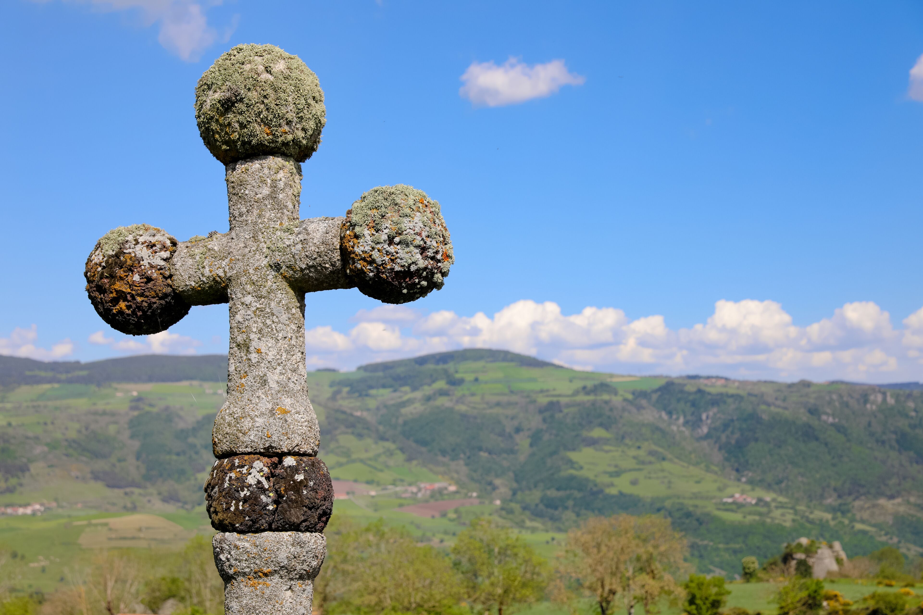 Croix de pierre au dessus d'une vallée en Haute Loire. Paysage de campagne vallonnée l'été en Auvergne. Nature, collines, forêts, champs et prairies à Charraix en France.