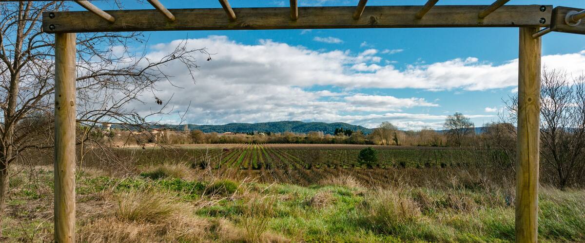 A wooden pergola in a field with mountains in the background.