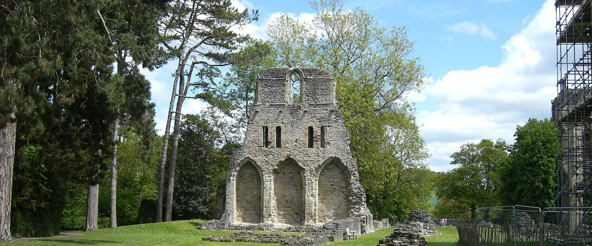 A historic stone structure with arched windows and a tower, surrounded by a well-maintained lawn and trees.