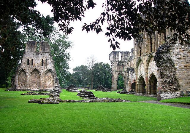 A historic castle ruin with arched windows and stone walls, surrounded by a well-maintained lawn and trees.