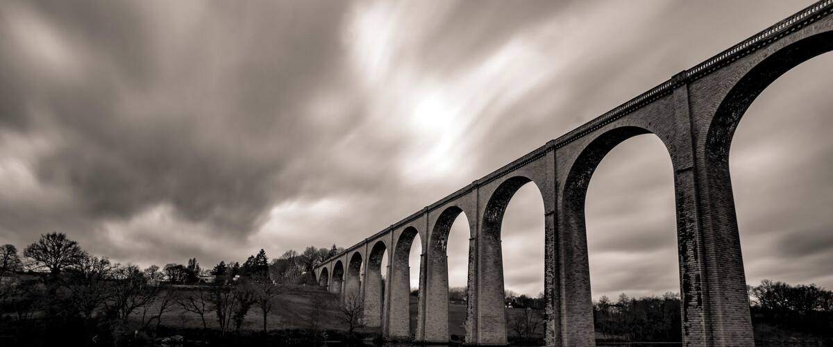 A long bridge with multiple arches spanning a calm body of water, reflecting the structure.
