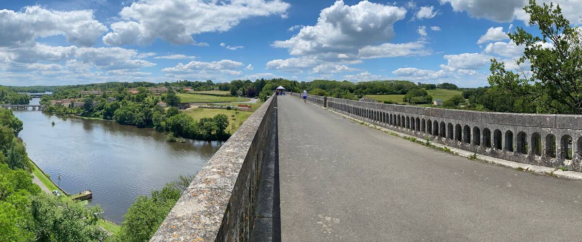 A river with a bridge, lush greenery, and a clear sky.