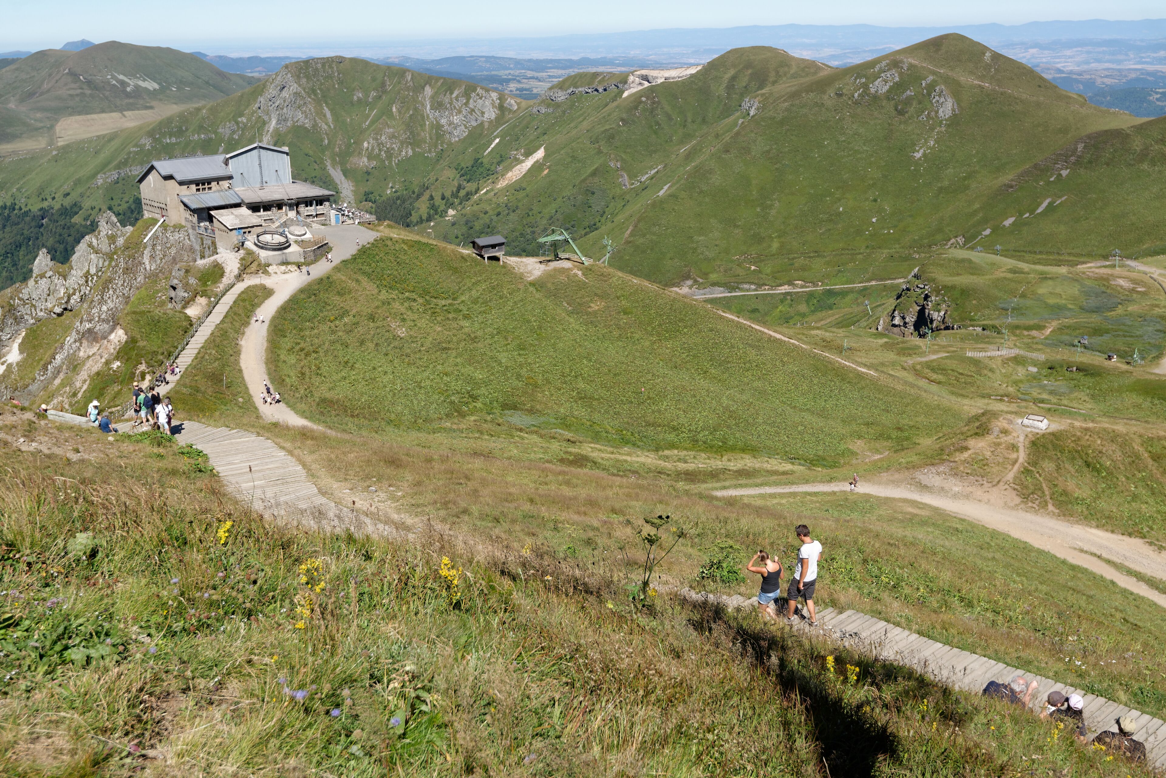 Un albergue de montaña con un camino sinuoso y una vista panorámica de colinas ondulantes.
