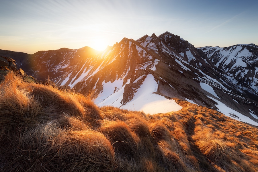 A mountain range with snow-covered peaks and a grassy foreground.