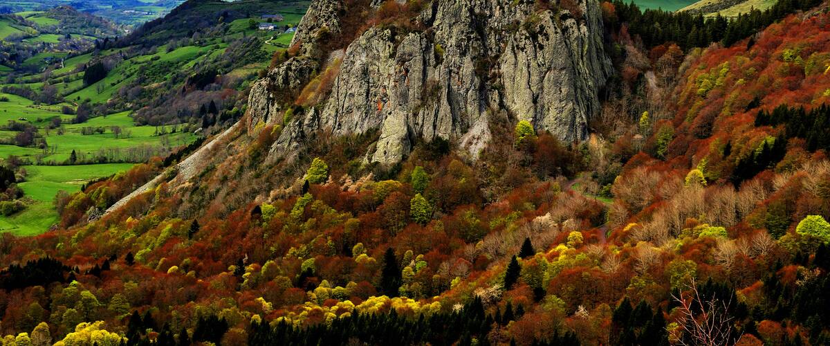 A rugged mountain peak with autumn foliage, surrounded by rolling hills and a distant valley.