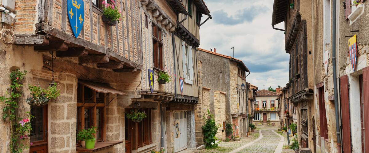A cobblestone street lined with historic buildings, some with balconies and flower pots.